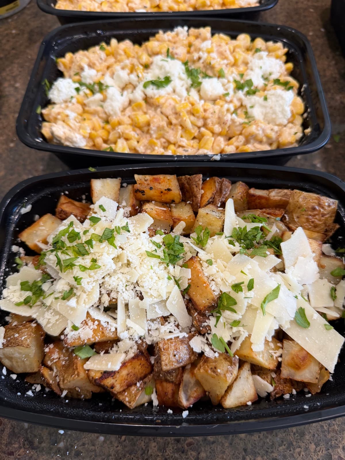 Meal-prep containers with parmesan potatoes and street corn